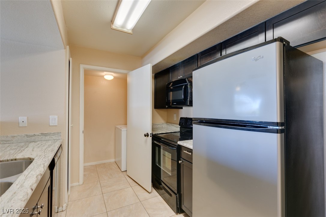 2300 East Silverado Ranch Boulevard, Unit 2190 Las Vegas, NV 89123 - Photo 29 of 41 Kitchen with black appliances, light tile patterned flooring, light stone countertops, and washer / clothes dryer