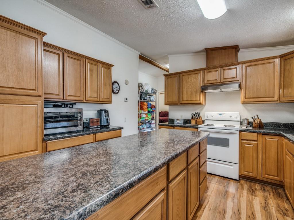 233 Esquire Estates Road Mabank, TX 75156 - Photo 11 of 34 Kitchen featuring electric range, light wood-style floors, ornamental molding, a textured ceiling, and brown cabinetry