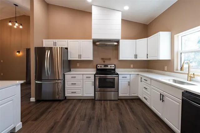 a kitchen with stainless steel appliances kitchen island granite countertop a refrigerator a sink dishwasher a stove and white countertops with wooden floor