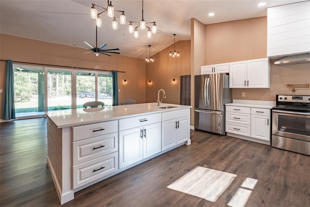6425 Cartwrite Road Spring Hill, FL 34609 - Photo 19 of 74 a kitchen with stainless steel appliances kitchen island granite countertop a refrigerator a sink dishwasher a stove and white countertops with wooden floor