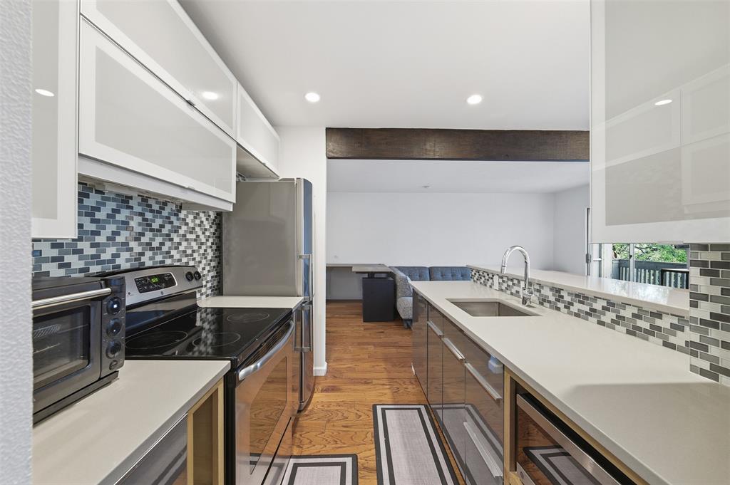 4837 Cedar Springs Road, Unit 311 Dallas, TX 75219 - Photo 9 of 17 Two tone kitchen featuring tasteful backsplash, stainless steel appliances, light wood-type flooring, beamed ceiling, and recessed lighting