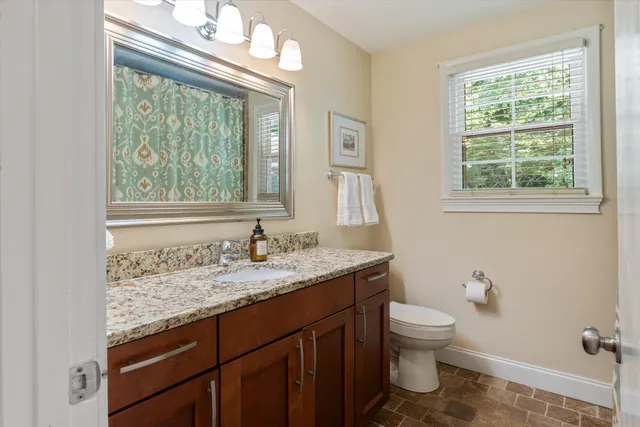 a bathroom with a granite countertop toilet a sink a mirror and a window