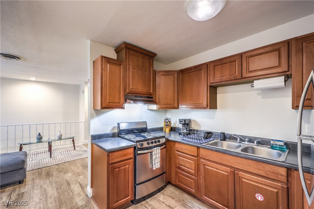 1553 Dorothy Avenue, Unit 4 Las Vegas, NV 89119 - Photo 11 of 36 Kitchen with stainless steel appliances, brown cabinets, dark countertops, light wood-style flooring, and a textured ceiling