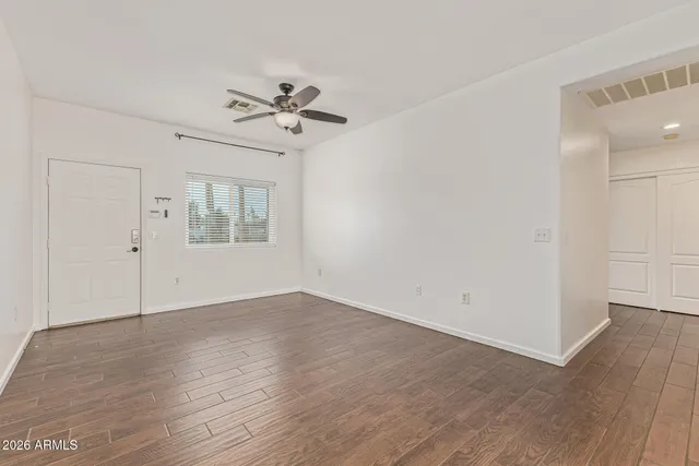 an empty room with wooden floor chandelier fan and windows
