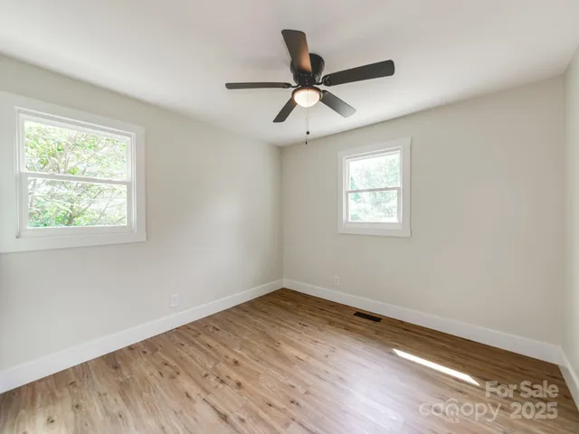 a view of empty room with wooden floor and fan