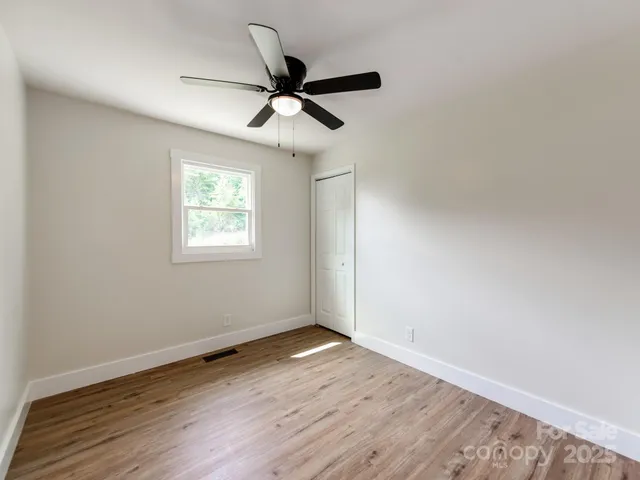 an empty room with wooden floor ceiling fan and window