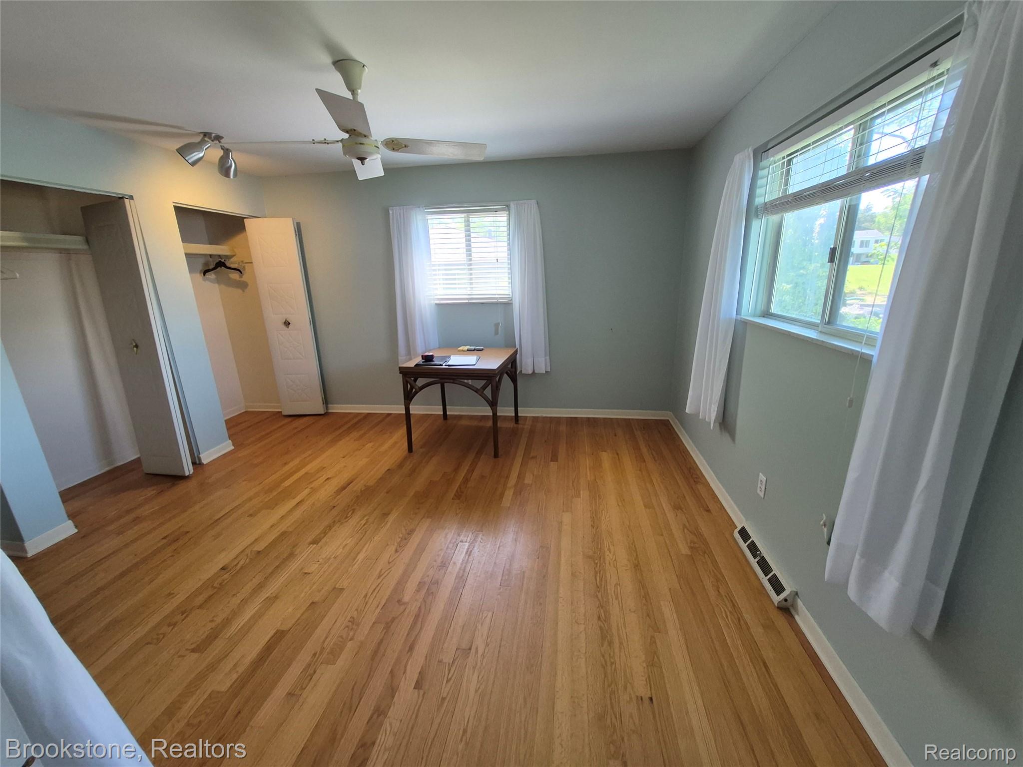 4295 Sashabaw Road Waterford, MI 48329 - Photo 19 of 37 Hardwood flooring throughout this room, featuring two windows with blinds and sheer curtains