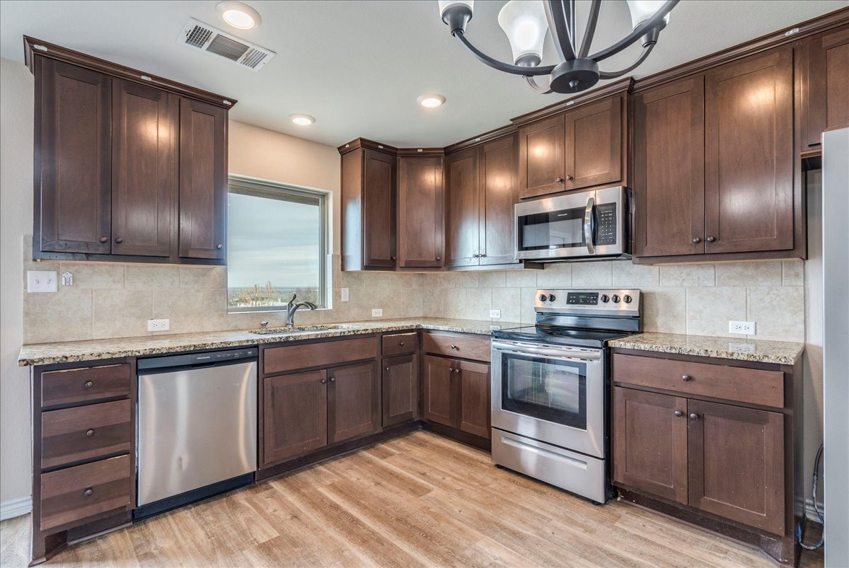 1092 Engelke Road Niederwald, TX 78640 - Photo 9 of 24 a kitchen with stainless steel appliances granite countertop wooden cabinets a sink and a stove
