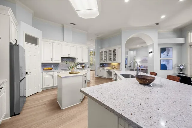 a kitchen with stainless steel appliances granite countertop a sink dishwasher a refrigerator and white cabinets with wooden floor