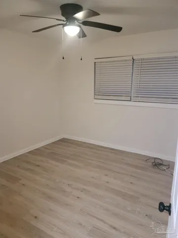 a view of an empty room with wooden floor and fan