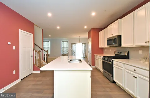 a kitchen with stainless steel appliances kitchen island granite countertop a refrigerator a stove top oven a sink dishwasher and white cabinets with wooden floor