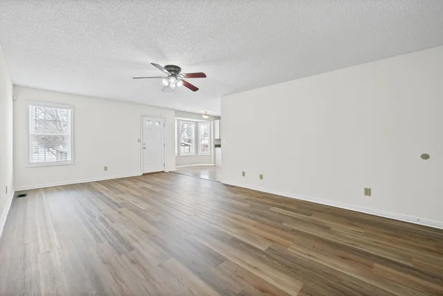 an empty room with wooden floor ceiling fan and windows