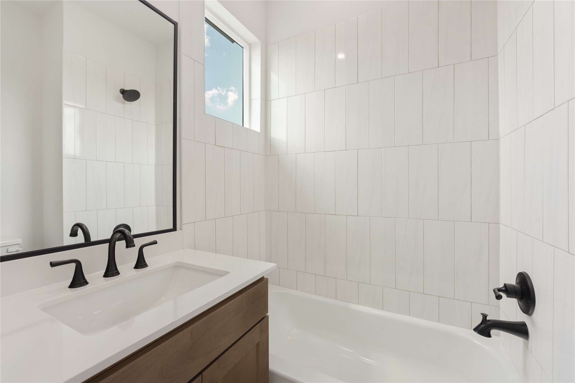 2121 Hoskins Drive, Unit C Houston, TX 77080 - Photo 31 of 34 Secondary bath with a fresh modern design featuring a wood vanity, white countertop, black fixtures, framed mirror, tub/shower combination, and vertical tile surround. A high window brings in natural light, while the clean finishes and crisp contrast create a polished, functional bath.