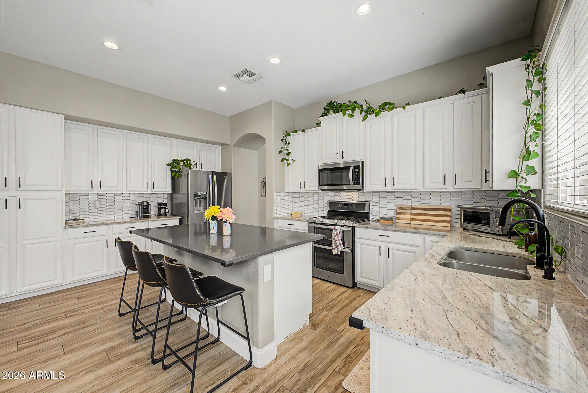 4272 East Buckboard Road Gilbert, AZ 85297 - Photo 15 of 37 a kitchen with stainless steel appliances kitchen island granite countertop a stove top oven a sink a refrigerator white cabinets and wooden floor