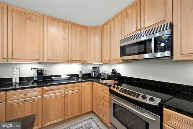 a kitchen with stainless steel appliances granite countertop a refrigerator a sink a stove and wooden cabinets