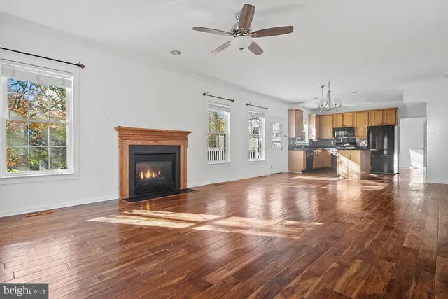 a view of a livingroom with a fireplace a ceiling fan and wooden floor