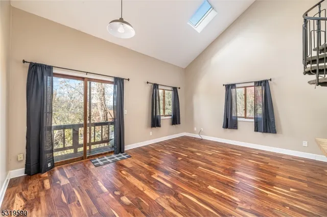 a view of an empty room with window and hardwood floor