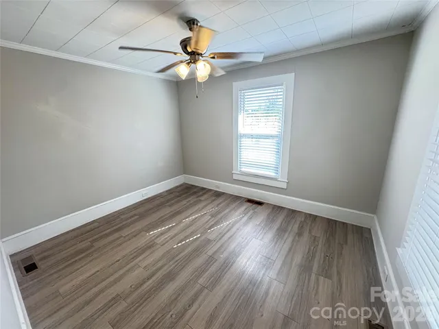 an empty room with wooden floor fan and windows