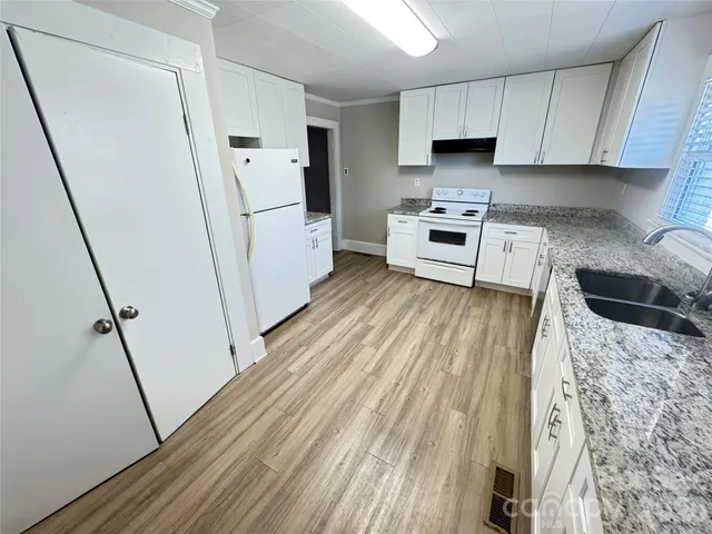 a kitchen with granite countertop a refrigerator a sink and white cabinets