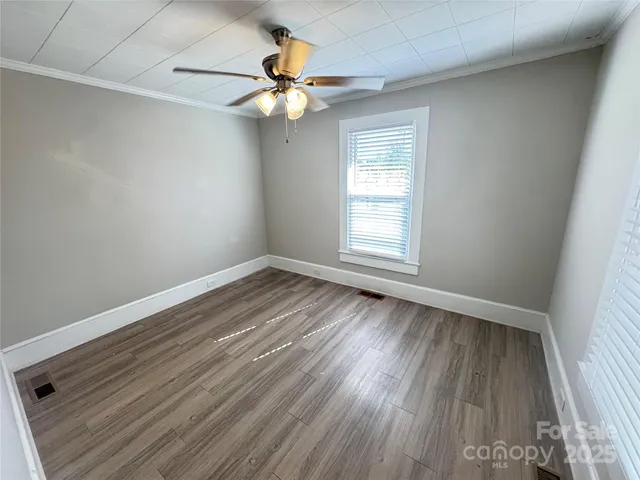an empty room with wooden floor fan and windows