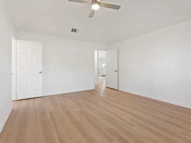 an empty room with wooden floor fan and windows