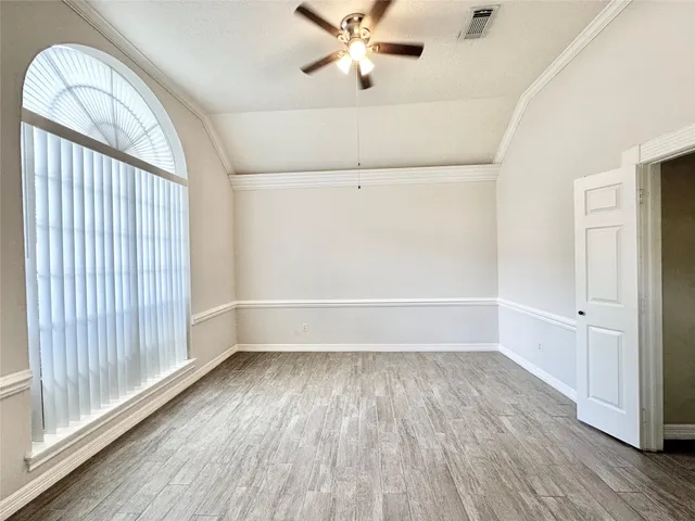 an empty room with wooden floor fan and windows