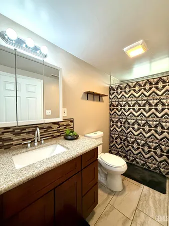a bathroom with a granite countertop toilet a sink a mirror a shower and a window