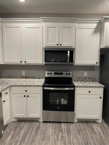 a kitchen with granite countertop a stove a microwave and white cabinets