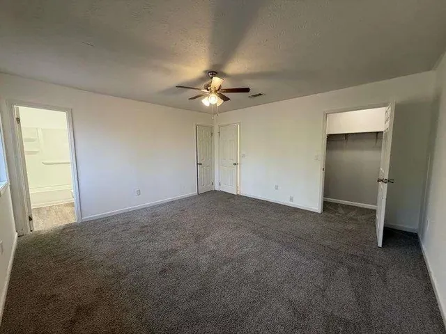 an empty room with chandelier fan and windows
