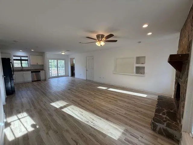 a view of an empty room with wooden floor and a kitchen