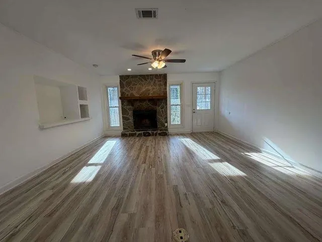 an empty room with wooden floor fireplace and windows