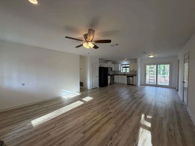 a view of an empty room and a kitchen with wooden floor and a ceiling fan