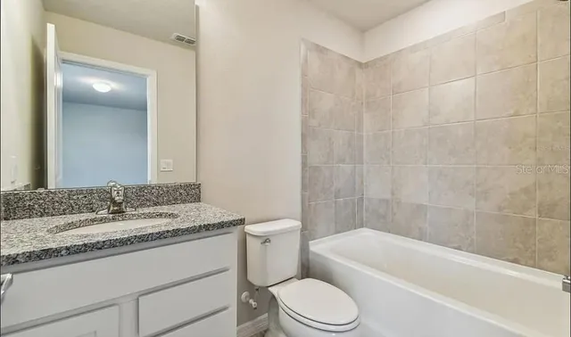 a bathroom with a granite countertop sink a toilet a mirror and bathtub