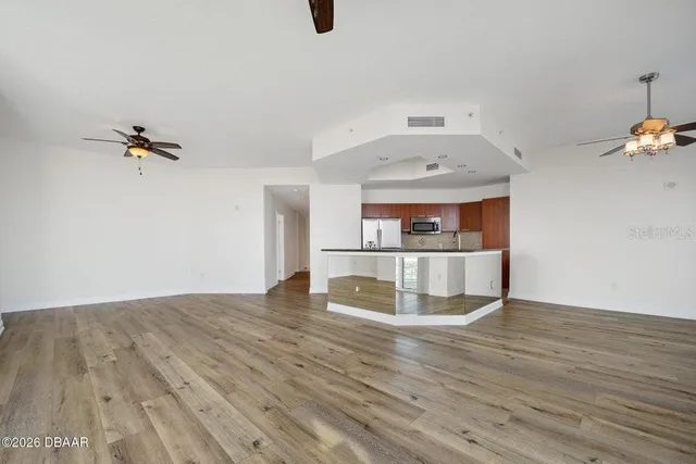 an empty room with wooden floor fan and windows