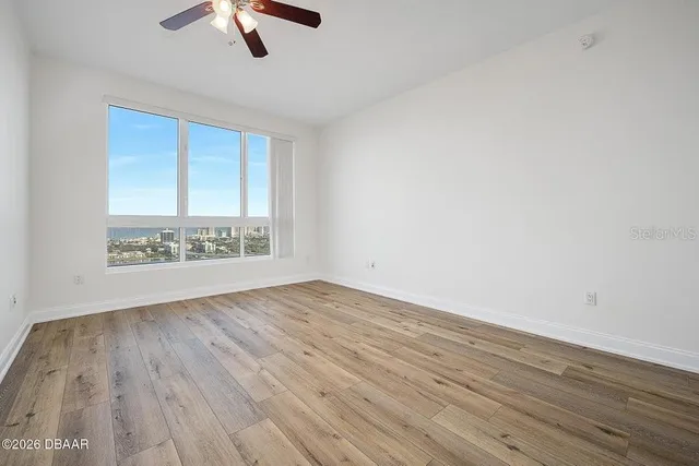 an empty room with wooden floor fan and windows