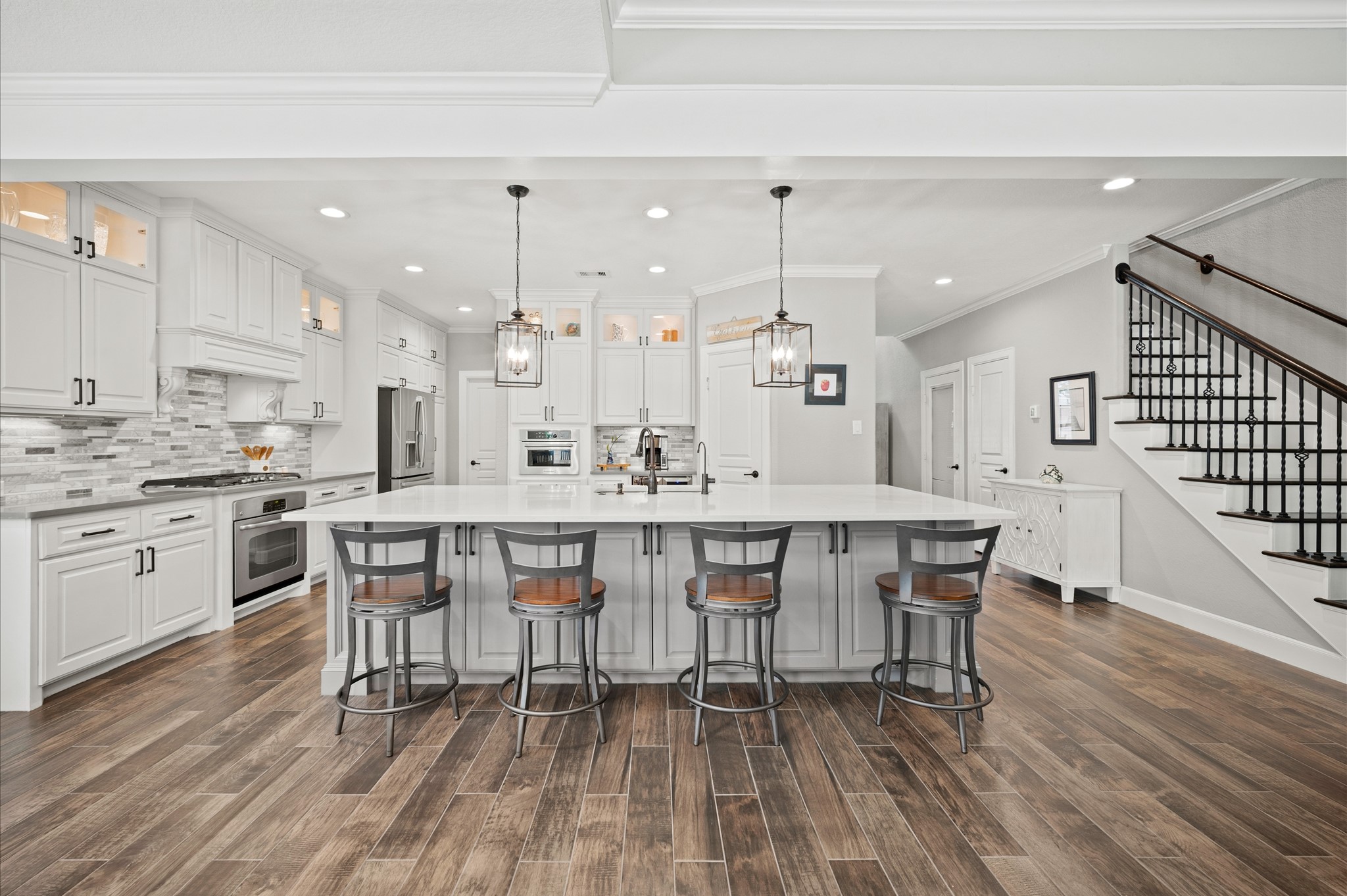 9507 Empress Crossing Drive Spring, TX 77379 - Photo 12 of 50 This spacious kitchen features modern white cabinetry, a large central island with seating, and pendant lighting. The open layout includes stainless steel appliances, a tile backsplash, and wood flooring, creating a stylish and functional space.