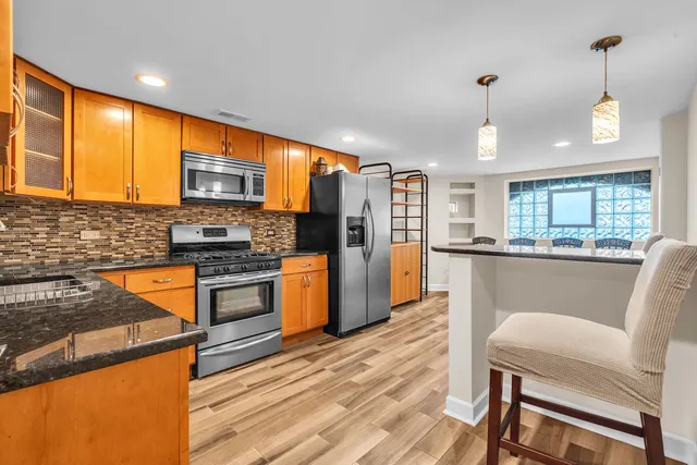 a kitchen with stainless steel appliances granite countertop a refrigerator a stove top oven a sink dishwasher and wooden cabinets with wooden floor