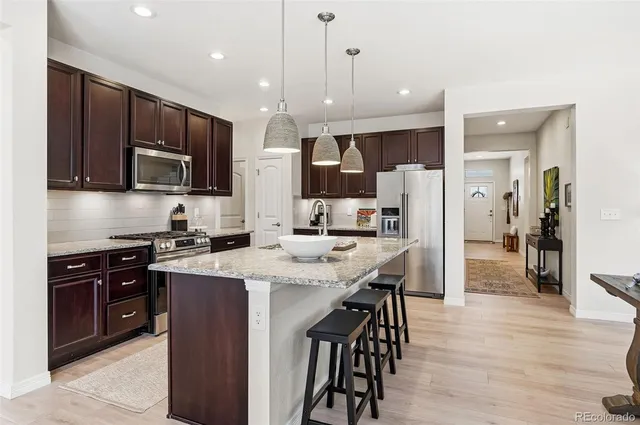a kitchen with stainless steel appliances kitchen island granite countertop a refrigerator a stove a sink a dining table and chairs with wooden floor