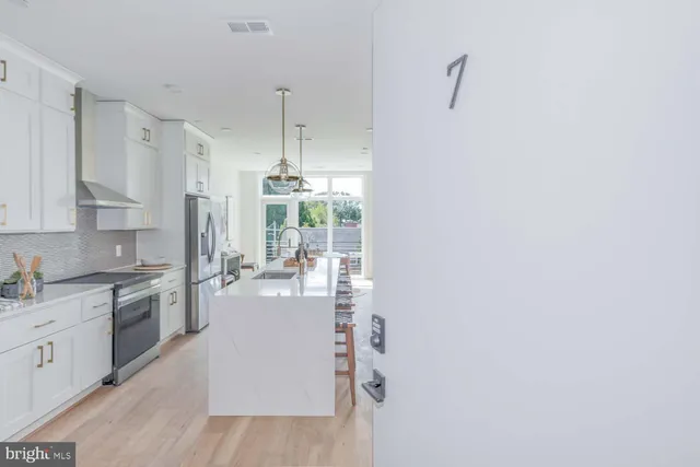 a kitchen with stainless steel appliances a refrigerator a sink dishwasher a stove and white cabinets with wooden floor