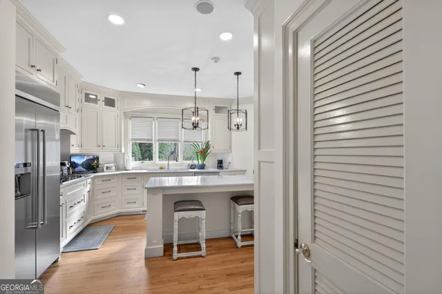 a kitchen with stainless steel appliances granite countertop a refrigerator a sink dishwasher a stove a dining table and chairs with wooden floor