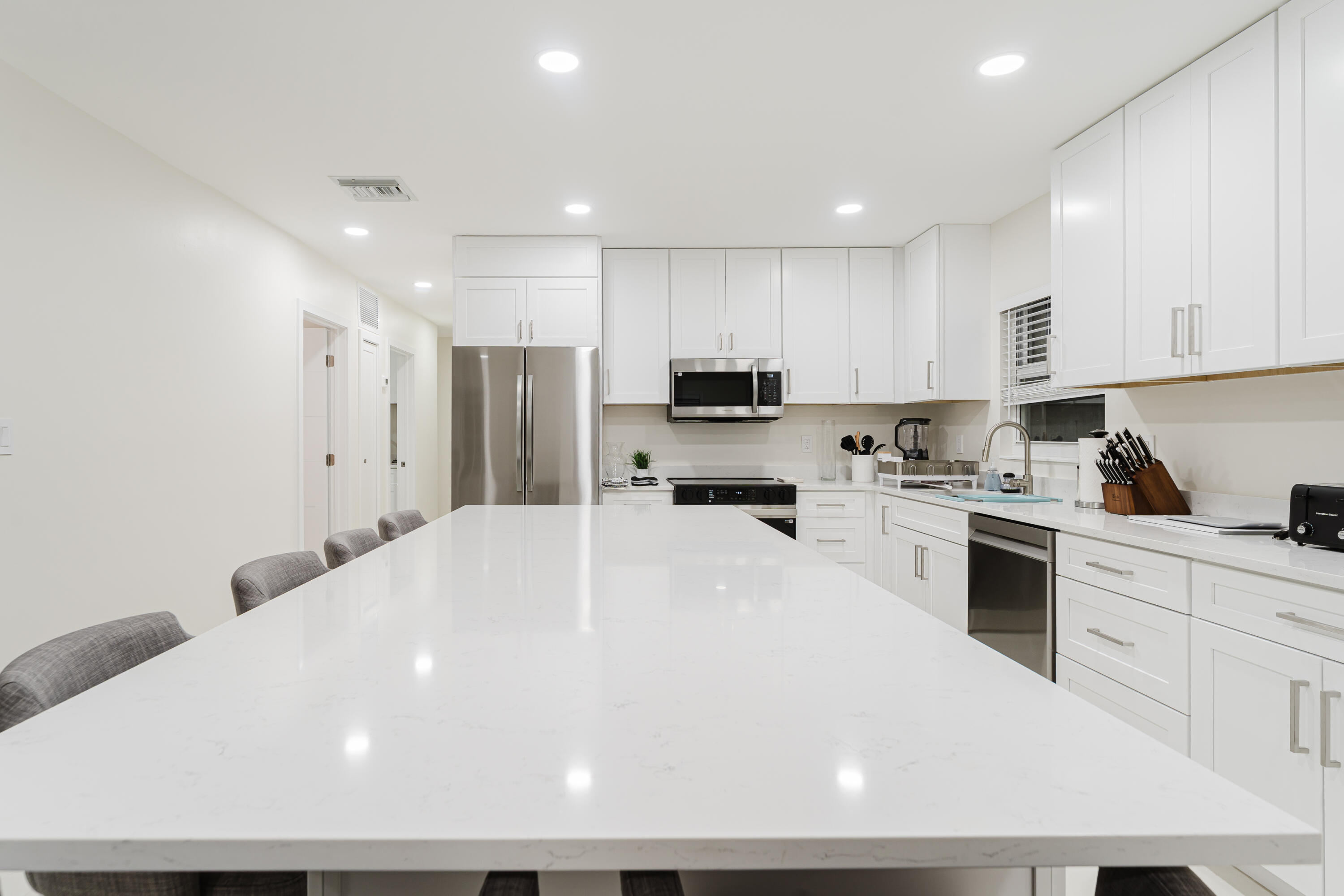 3199 Northeast 6th Drive Boca Raton, FL 33431 - Photo 19 of 49 a large white kitchen with stainless steel appliances a large counter top a stove a sink a refrigerator and a refrigerator