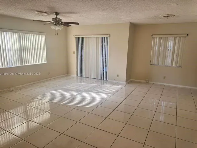 a view of an empty room with window and chandelier fan