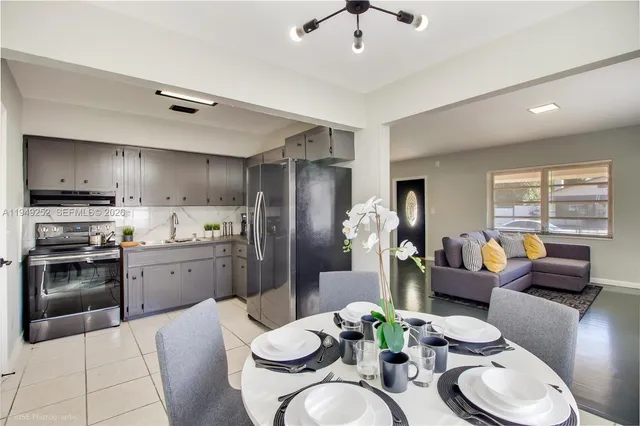 a kitchen with stainless steel appliances granite countertop a refrigerator a sink dishwasher a dining table and chairs with wooden floor