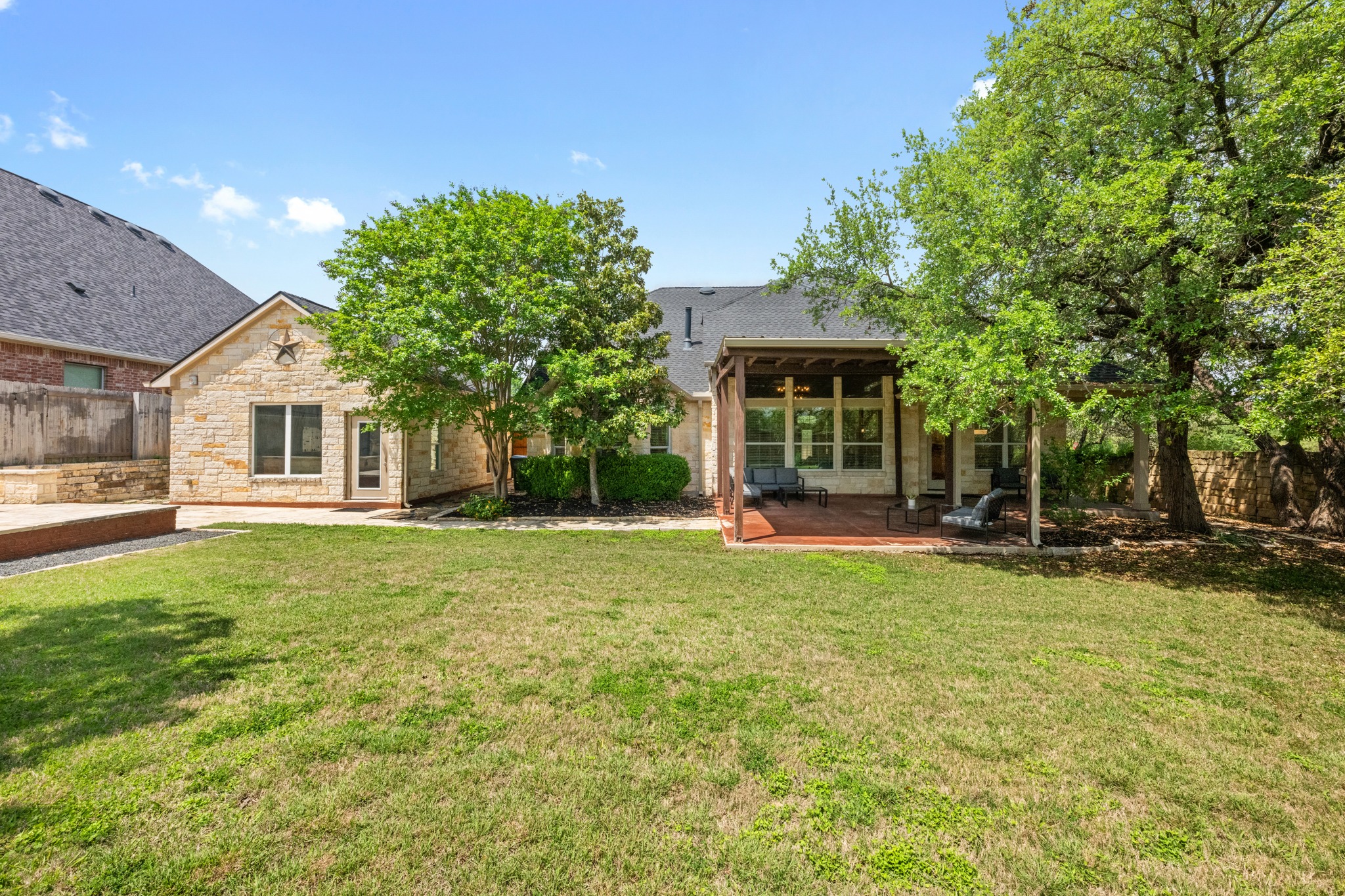 1023 Grassy Field Road Austin, TX 78737 - Photo 34 of 40 Expansive backyard featuring a manicured lawn, stone retaining wall, and mature trees. Enough space for a pool.