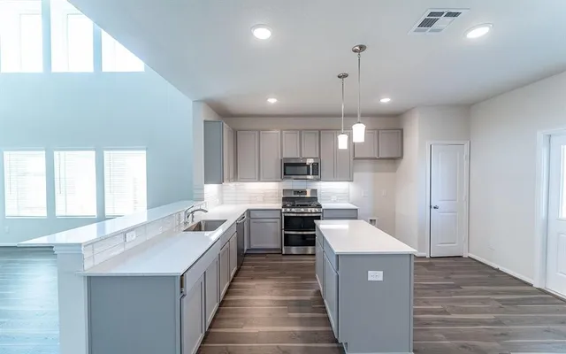 a large kitchen with stainless steel appliances kitchen island granite countertop a large stove a sink dishwasher and a refrigerator with wooden floor