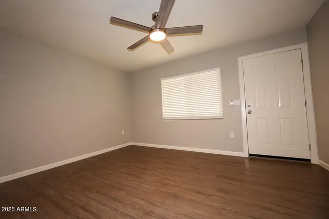 an empty room with wooden floor ceiling fan and windows