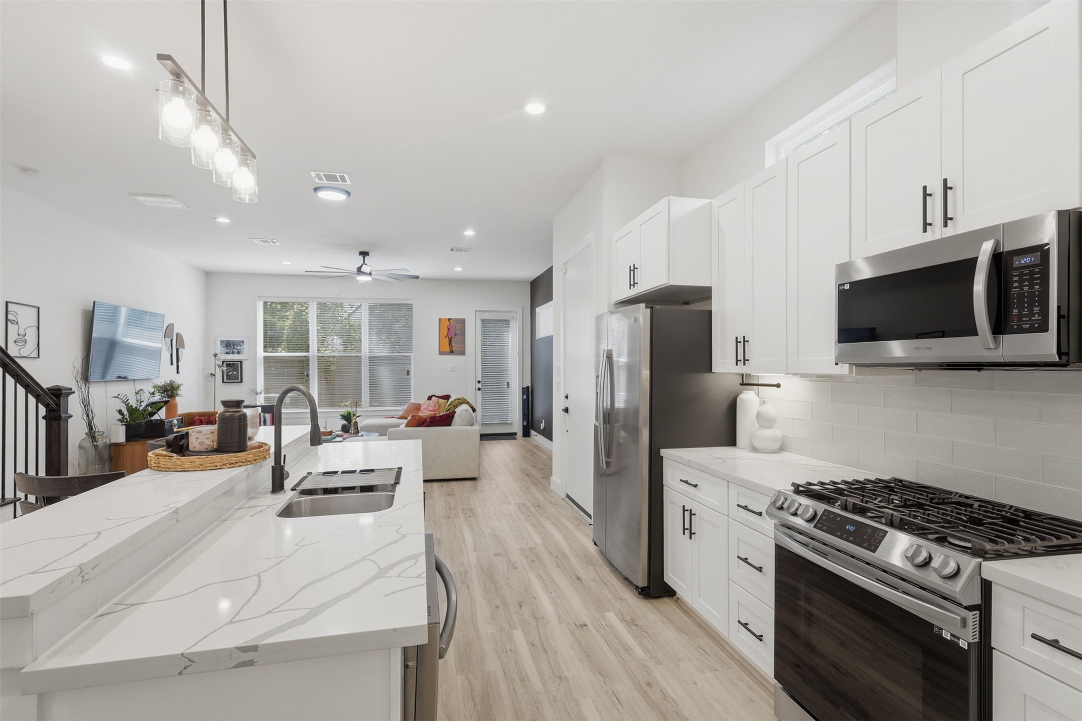 6833 Paris Street Houston, TX 77021 - Photo 7 of 23 This modern kitchen and living area features sleek white cabinets, stainless steel appliances, and a spacious open layout. The room is bright and airy with large windows and light wood flooring, providing a welcoming ambiance.