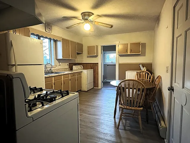 a kitchen with stainless steel appliances a refrigerator a sink a stove top oven a dining table and chairs with wooden floor