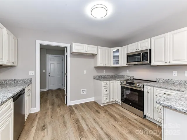 a kitchen with stainless steel appliances granite countertop a stove top oven a sink dishwasher and a microwave oven with white cabinets