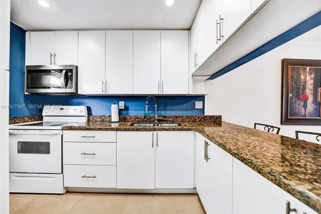 a kitchen with granite countertop a sink stainless steel appliances and white cabinets